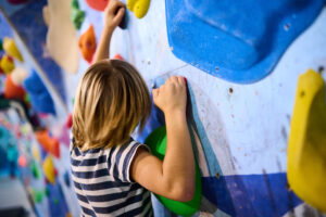 a 6 year old boy climbing on a vibrant indoor bouldering wall with multicolored holds, engaging in a fun and active climbing experience. perfect for kids fitness and adventure